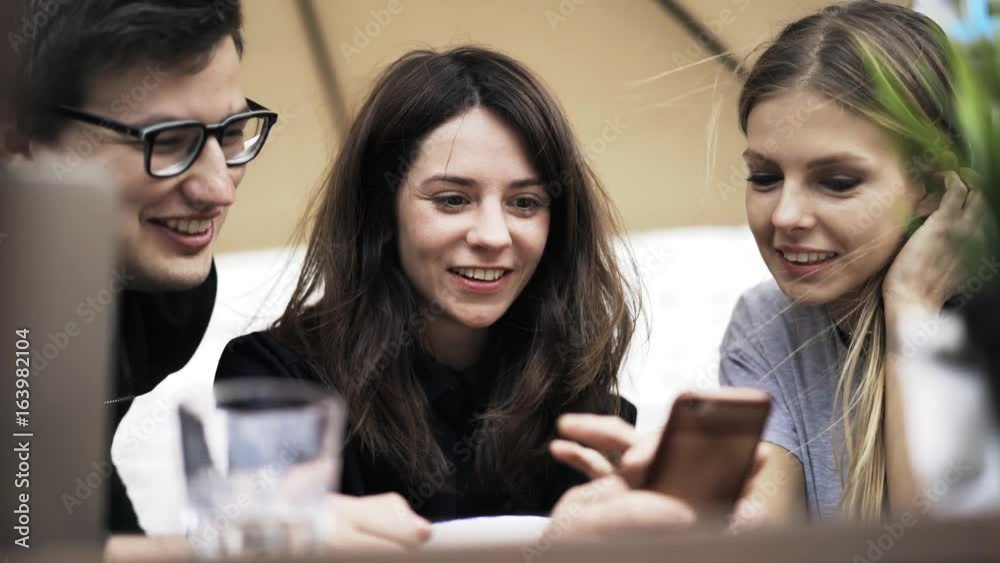 Front view of three young people having a video chat conversation with their fourth friend with a smartphone. Handheld real time close up shot Front view of three young people having a video chat conversation with their fourth friend with a smartphone. Handheld real time close up shot