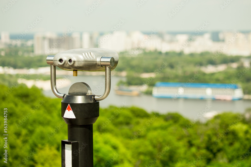 Stationary observation binoculars , metropolis landscape on the background with bridge, river, boats, subway, and scyscrapers Stationary observation binoculars , metropolis landscape on the background with bridge, river, boats, subway, and scyscrapers