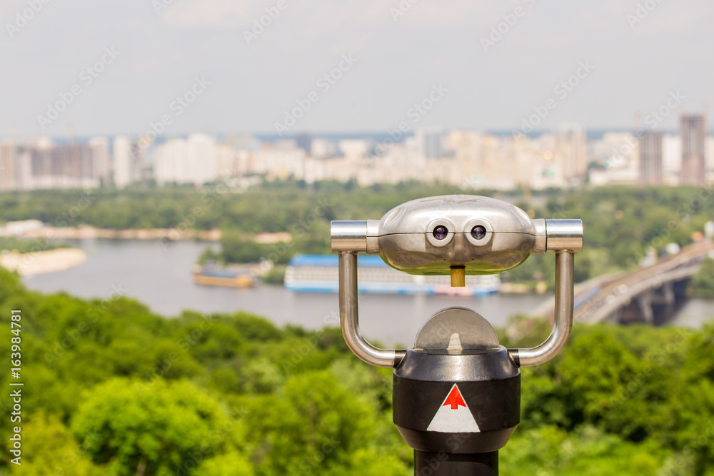 Stationary observation binoculars , metropolis landscape on the background with bridge, river, boats,  subway, and scyscrapers
