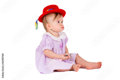 Lovely baby in colored dress and red hat are playing on a white background