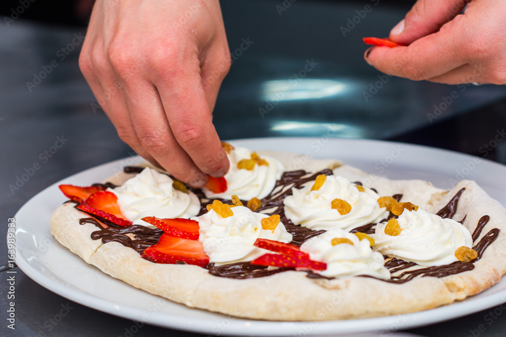 cooking of sweet Italian pizza. Hands pizza maker put on the cream berries, raisins, strawberries