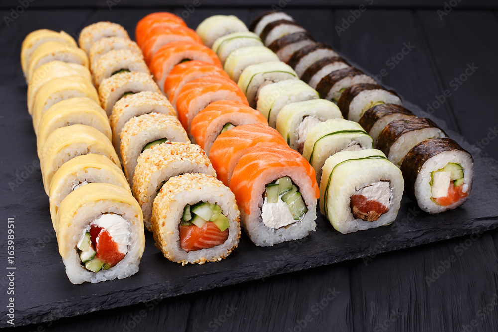 Delicious fresh multicolored sushi set on black slate, close-up. Traditional japanese food, restaurant serving Delicious fresh multicolored sushi set on black slate, close-up. Traditional japanese food, restaurant serving
