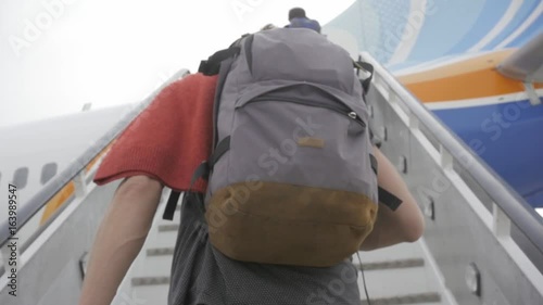 Young man passenger in airport travelling with backpack, boarding airplane, people climbing ramp on background, rear view photo