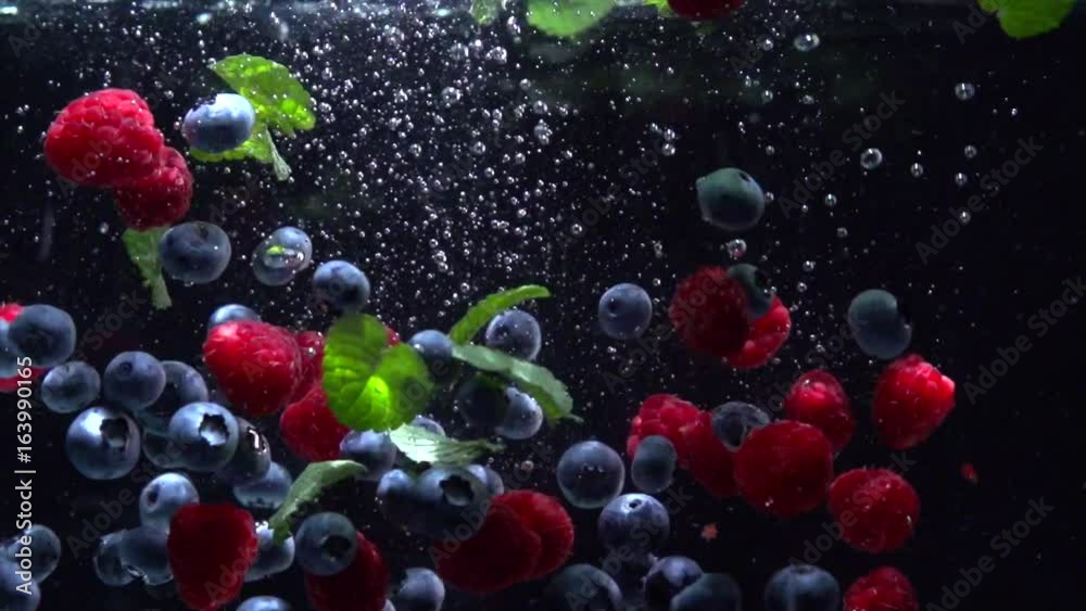 Raspberry and blueberry. Berries splashing into water on black background. 4K UHD video 3840X2160 slow motion