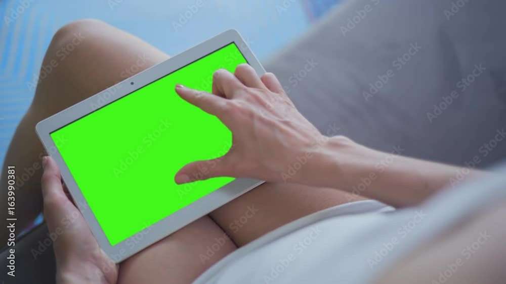Young Woman in white top sitting on sofa uses Tablet PC with pre-keyed green screen. Few types of gestures - scrolling up and down, tapping, zoom in and out. Perfect for screen compositing
