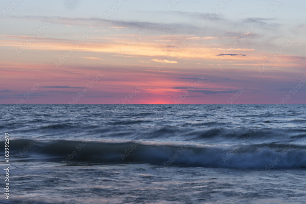 Smooth waves rolling in and crashing on sea under a pastel sky just after sunset Smooth waves rolling in and crashing on sea under a pastel sky just after sunset