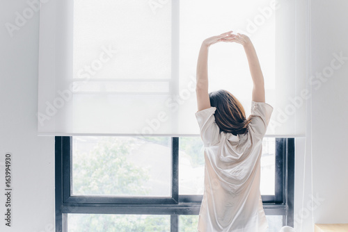 Free Download Asian woman stretching near the window after her wake up in the morning, back view. - GFXLoad