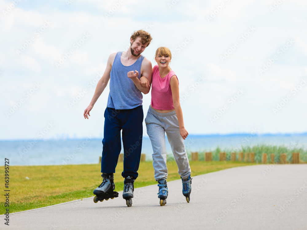 Fototapeta premium Young couple holding hands while rollerblading