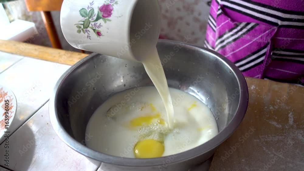 Preparation for kneading the dough. The basis of the dough. Pouring milk into a metal bowl with eggs. uhd realtime video. Preparation for kneading the dough. The basis of the dough. Pouring milk into a metal bowl with eggs. uhd realtime video.