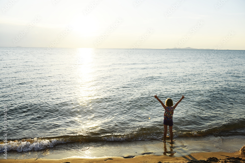 Silhouette rear view of young caucasian girl with arms raised at the beach alone