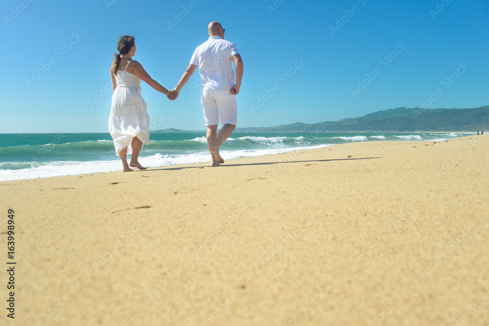 Young romantic couple walking on the beach holding hands Young romantic couple walking on the beach holding hands
