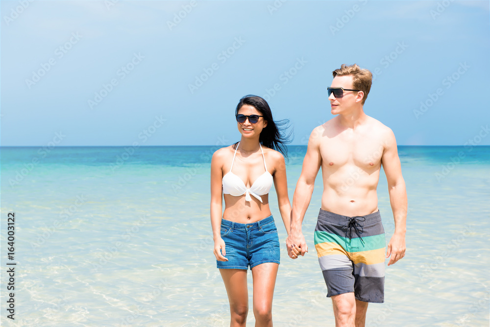 Interracial tourist couple walking on the beach in summer Interracial tourist couple walking on the beach in summer