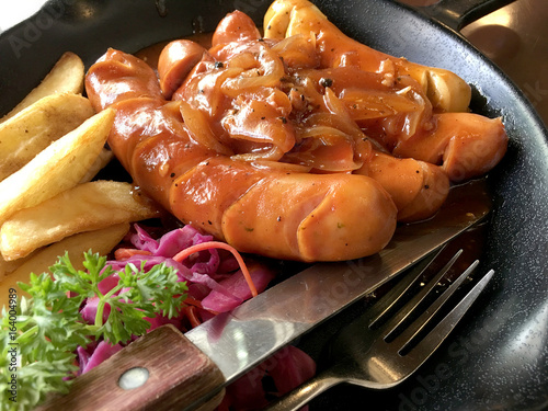 Fried sausages with garlic, herbs and french fries in a pan. On the table black Board. still life food. photo