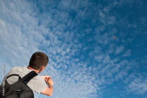 Young man with a backpack holding kite flying in a blue sky