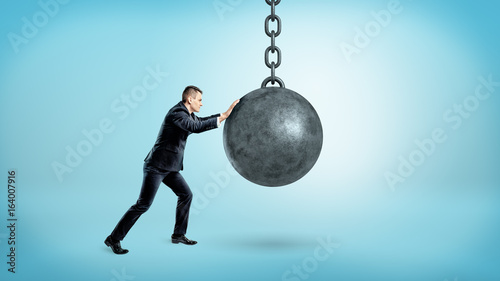 Canvas Print A businessman on blue background pushing at a hanging unmoving wrecking ball
