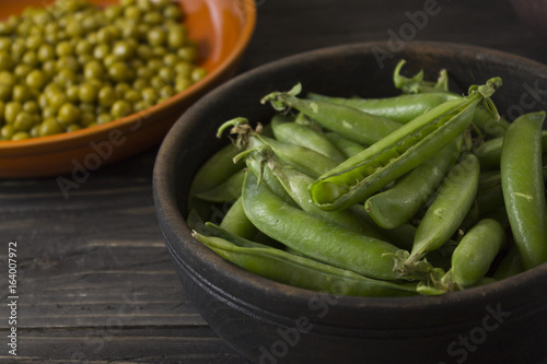 Fresh green peas in a wooden bowl and canned peas in a clay bowl on a wooden table. Healthy food.