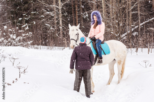 Girl, horse trainer and white horse in a winter