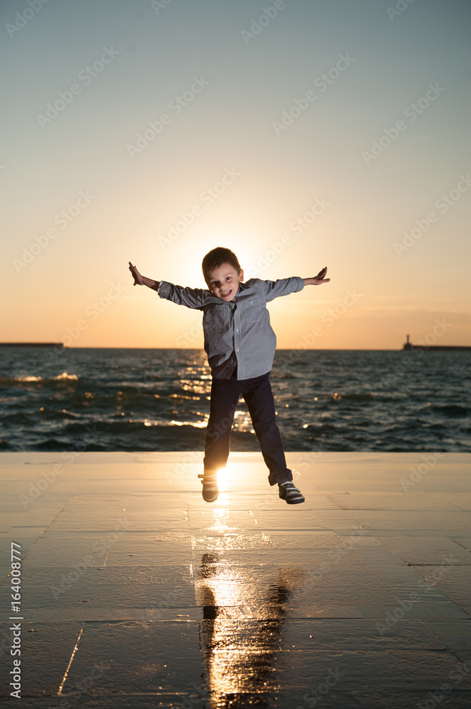 happy overjoyed little boy jumping on sea sunset background