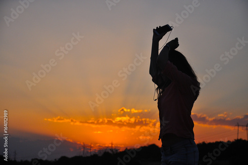 Silhouette of Young Attractive Hipster Girl Listening Music On The Mobile Phone And Dance At Sunset