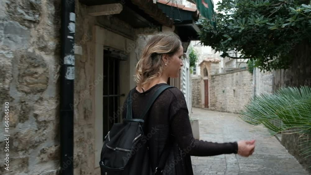 Young blonde woman walks on the street with stone buildings Young blonde woman walks on the street with stone buildings