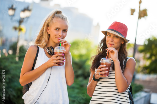 Two happy women are having nice time together in the city. They are drinking smoothie.