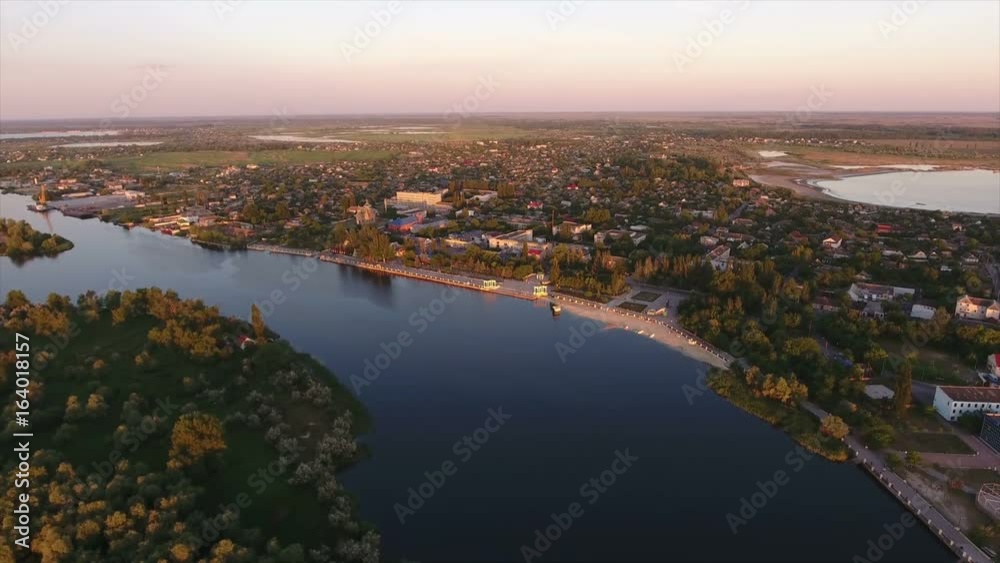 Astonishing view on the curvy Dnipro river with high trees, summer cottages, and green wetland at a picturesque sunset from a bird`s eye perspective. The skyscape with beaming rays looks gorgeous. Astonishing view on the curvy Dnipro river with high trees, summer cottages, and green wetland at a picturesque sunset from a bird`s eye perspective. The skyscape with beaming rays looks gorgeous.
