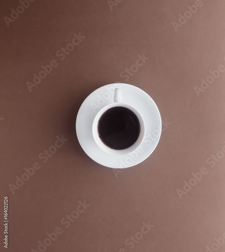 Hot black coffee in a white cup on gradient shade brown paper in top view.