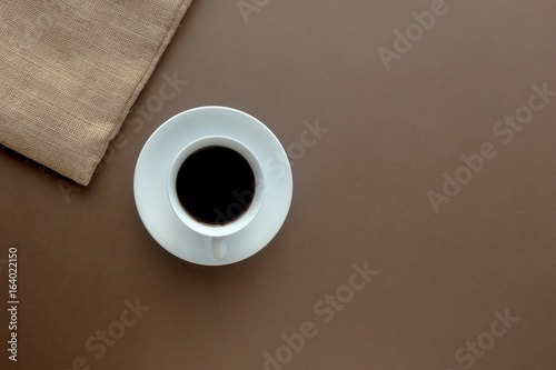 Hot black coffee in a white cup and sack on brown paper in top view.