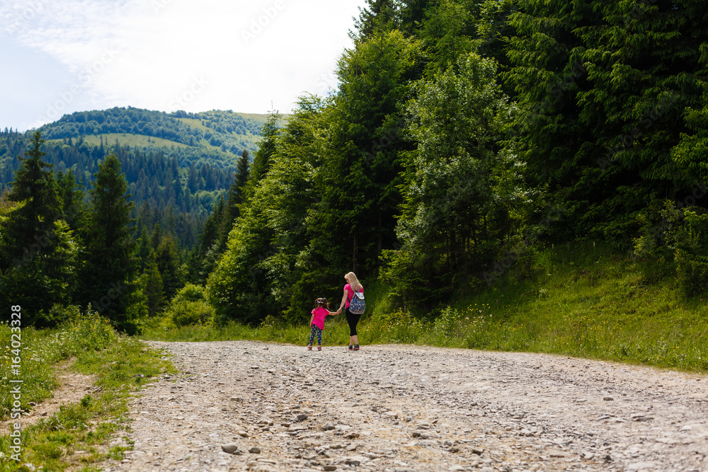 Mother and little girl walking along the mountain road