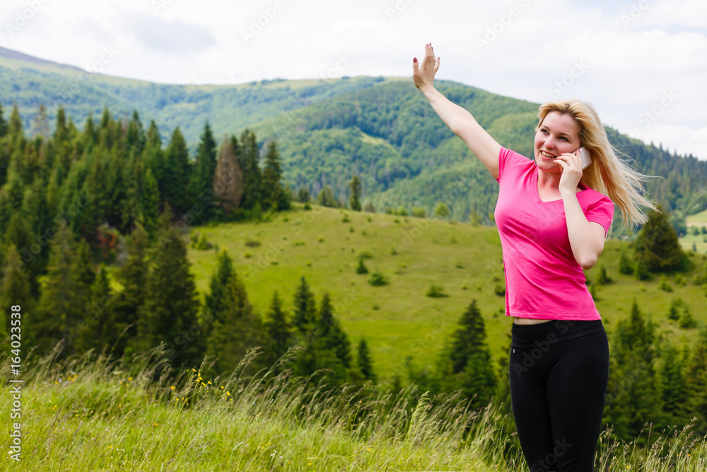 Cheerful smiling woman with mobile phone. Beautiful mountain meadows touristic path. Digital communication. Texting with friends in social network