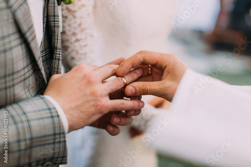 The close-up view of the priest putting the wedding ring on the finger of the groom. photo