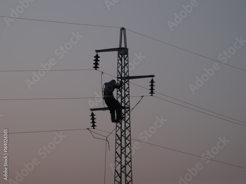 Silhouette of a worker on maintenance job on high voltage pole (power line pylon), featuring three phase wires shorted and grounded for security purposes