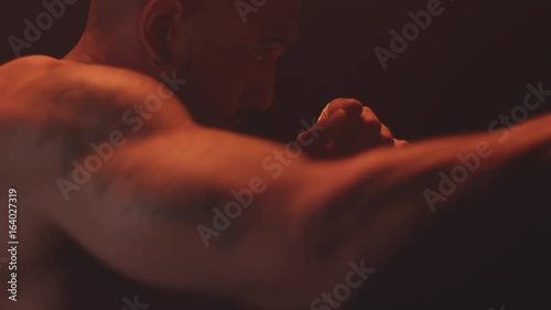 Profile shot of a muscular black man shadow boxing on a foggy dark red background 