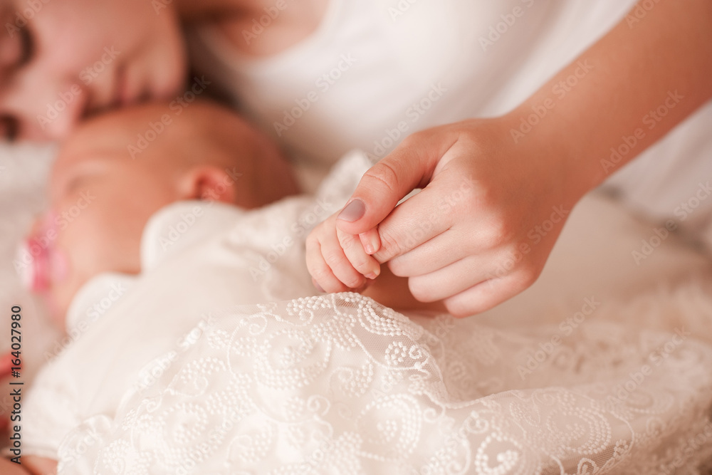 Sleeping infant baby lying in bed with mother holding small fingers closeup. Motherhood. Maternity. Healthy childhood. Selective focus. Sleeping infant baby lying in bed with mother holding small fingers closeup. Motherhood. Maternity. Healthy childhood. Selective focus.