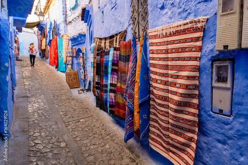 A vendor is selling carpets and blankets on a wall in Chefchaouen, Morocco © Deyan