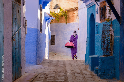 A woman dressed in hijab and sport clothing is walking down a street in Chefchaouen, Morocco