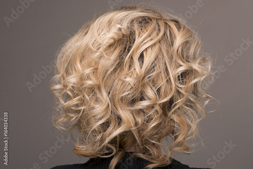 Bob cut hairstyle with short curls on the blonde on isolated grey background