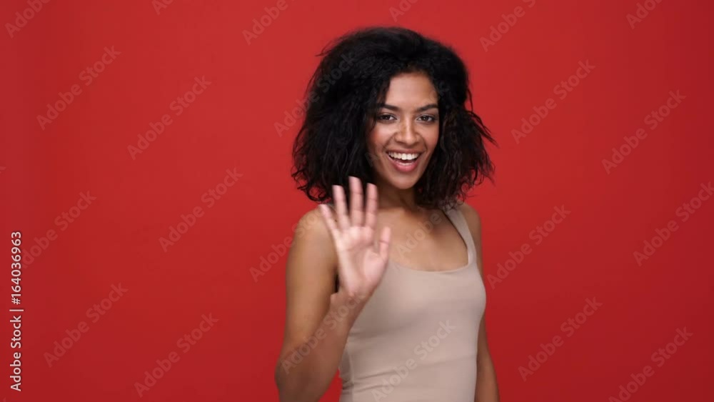 Young pretty african woman smiling and waving over red background Young pretty african woman smiling and waving over red background