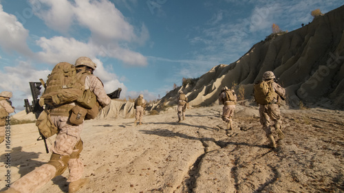 Shot of a Squad of Soldiers Running Forward and Atacking Enemy During Military Operation in the Desert. photo