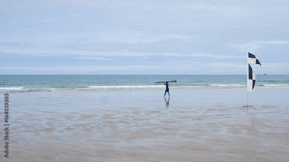 A surfer heads towards the water past a safety flag