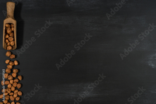 Hazelnuts in a wooden scoop on a black chalkboard.
