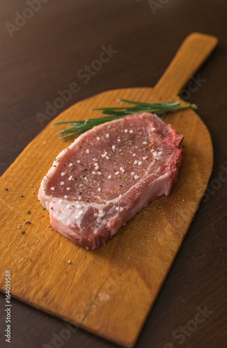 Raw pork steak with salt pepper ans rosemary on wooden board