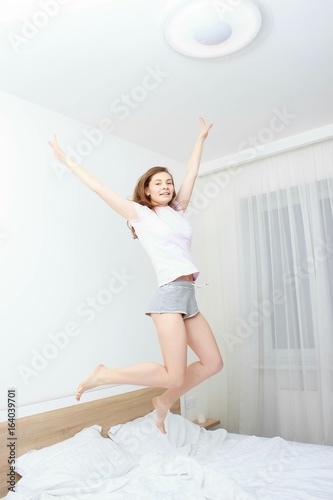 Portrait of a young happy woman jumping on bed