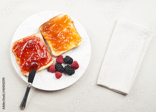 Top view of tasty toast breakfast with strawberry and peach jam along with blackberries and raspberries, and a napkin.