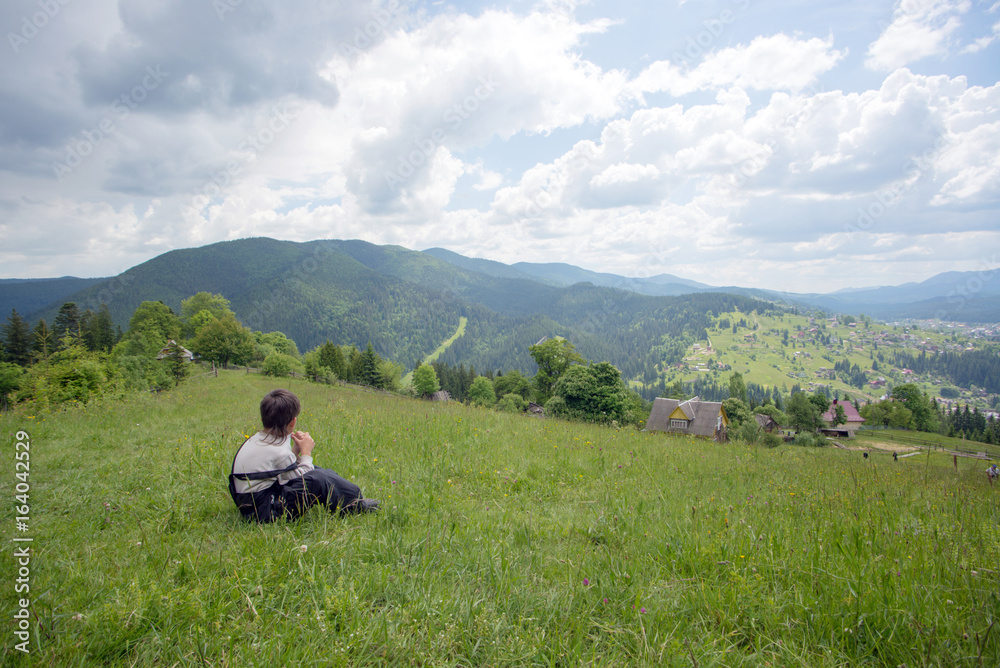 A boy sitting at the top of the hill and looking on mountains