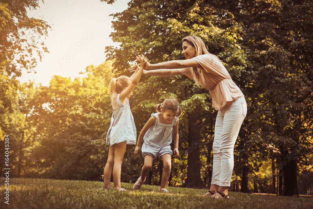 Fototapeta premium Mother with two child in meadow. Mother holding hands with girl other girls passing under the arm