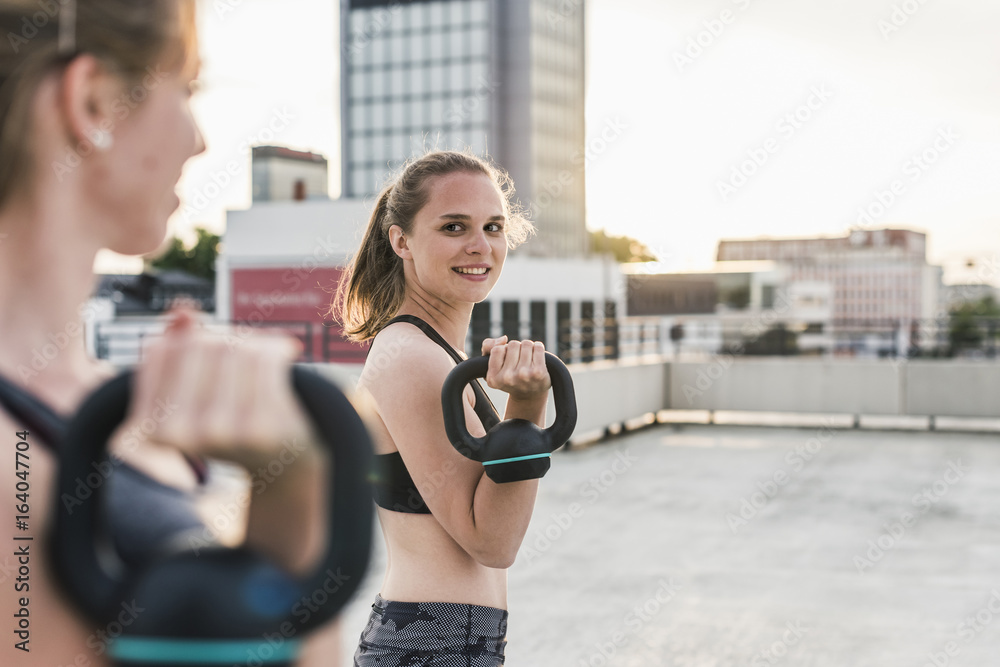 Two women exercising with kettlebells on parking level in the city