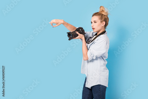 Woman blonde photographer shows how to pose to somebody. Model isolated on a blue background with copy space