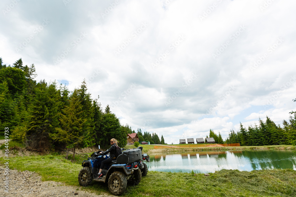 A happy woman riding a quad bike near a lake in the mountains A happy woman riding a quad bike near a lake in the mountains