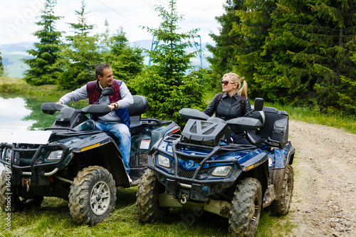 Young couple having fun on mountain while driving a quad bike on a summer day. Young man and woman on an ATV.